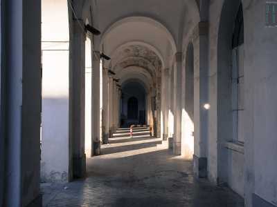 Tutto intorno si apre un lungo porticato costituito perlopi� da locali non utilizzati e murati, oppure usati come depositi. Qui le macchie di umidit� corrodono lo stucco alla base delle arcate e strisciano lungo le pareti per poi arricciarsi capricciosamente sul soffitto fino a creare improbabili affreschi